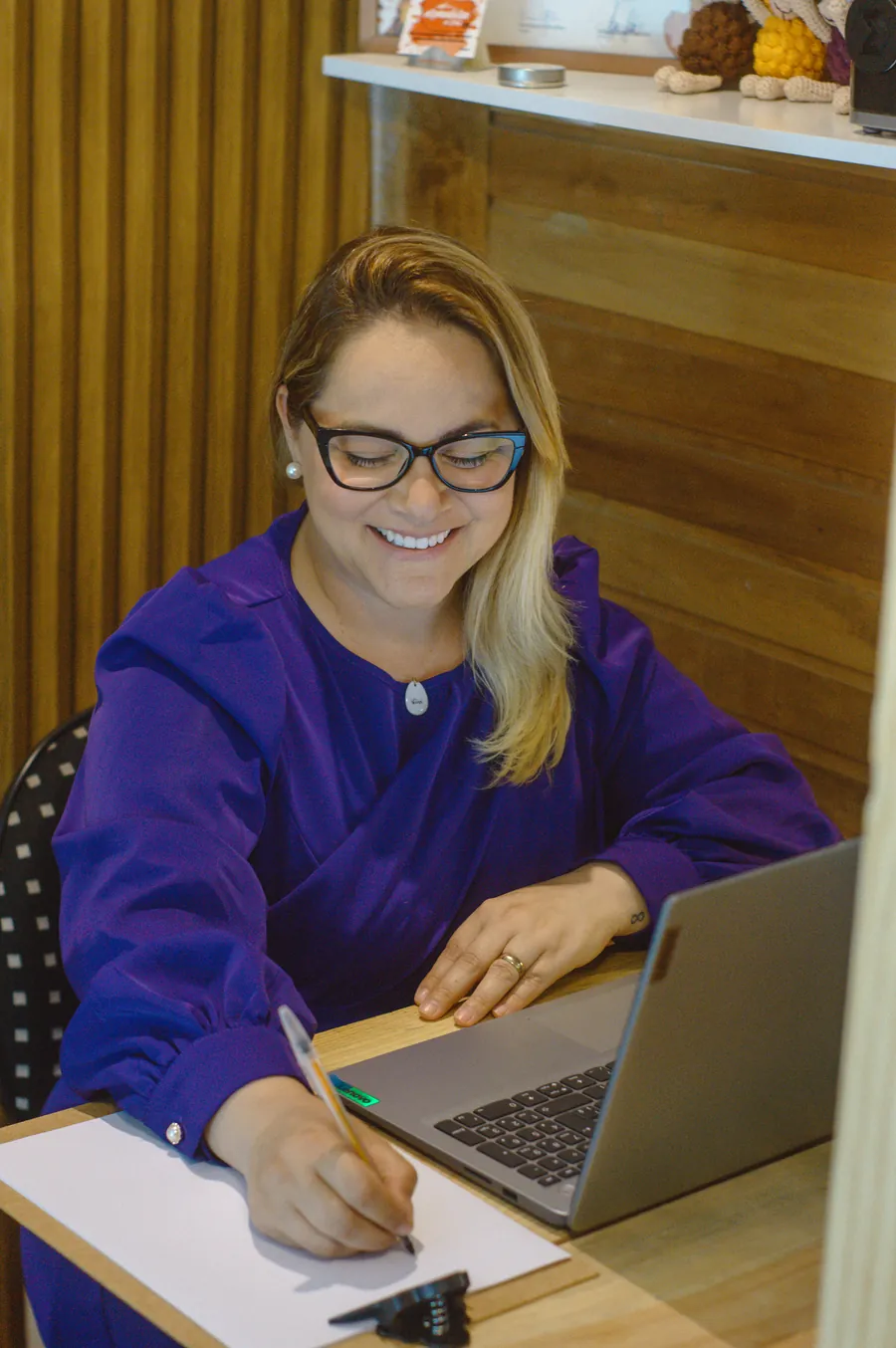 Viviane Saibro sorrindo enquanto faz anotações, com o notebook aberto